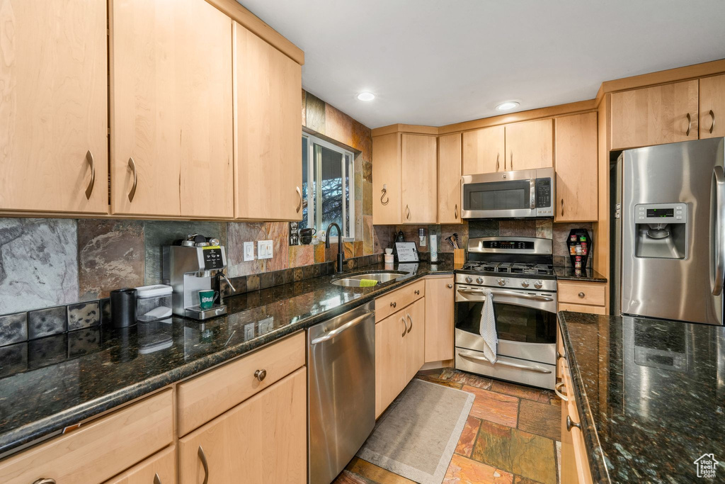 Kitchen featuring light brown cabinets, stainless steel appliances, a sink, decorative backsplash, and stone tile flooring