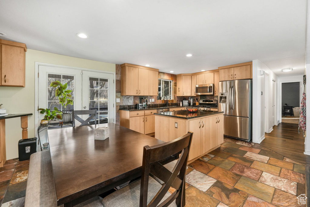 Kitchen with stone tile floors, dark countertops, stainless steel appliances, light brown cabinets, and a sink