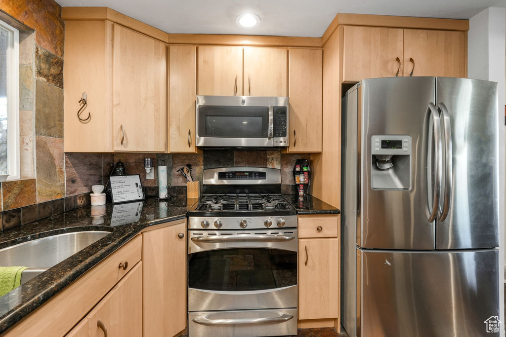 Kitchen with tasteful backsplash, light brown cabinets, and appliances with stainless steel finishes