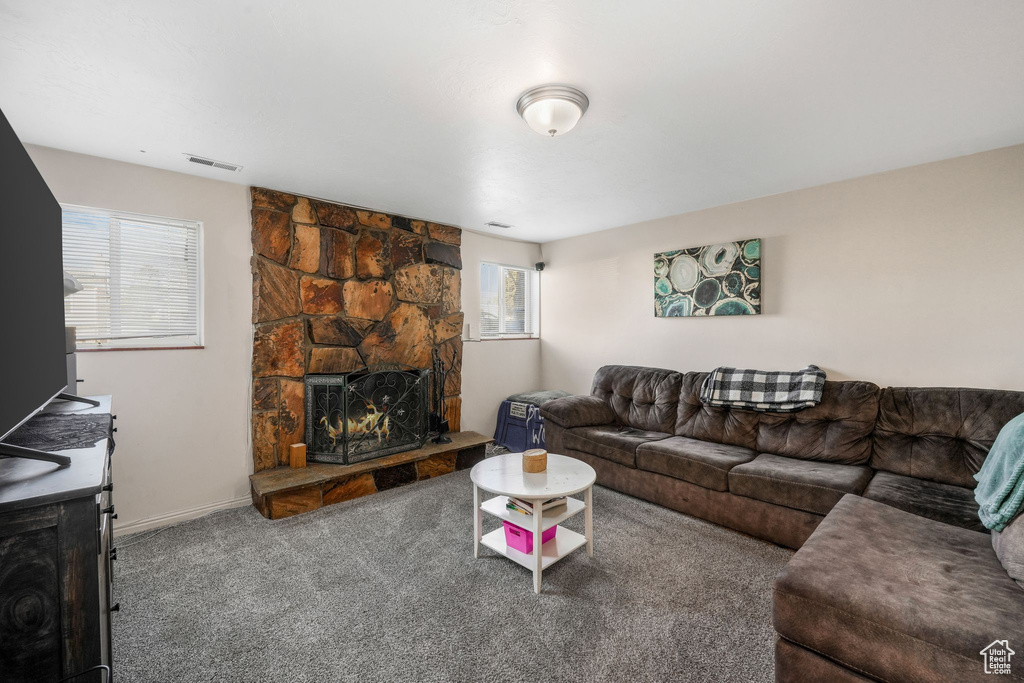 Living area featuring visible vents, carpet flooring, a stone fireplace, and baseboards