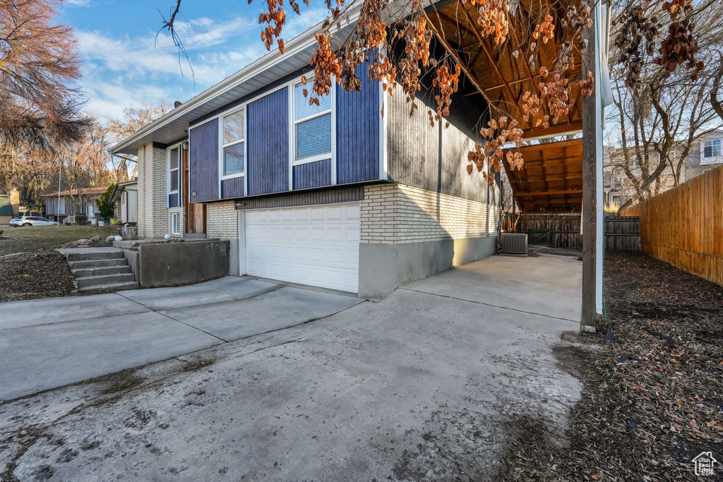 View of side of home featuring a garage, fence, concrete driveway, and brick siding