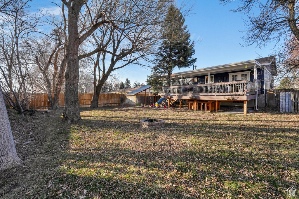 Rear view of house with an outdoor fire pit, a fenced backyard, a lawn, and a deck