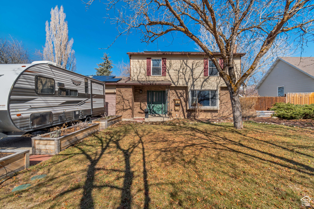 View of front of property featuring brick siding, a vegetable garden, a front yard, roof mounted solar panels, and fence