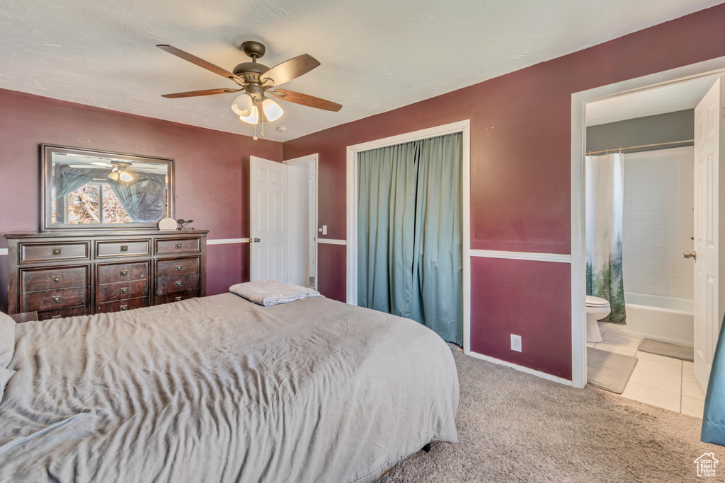 Carpeted bedroom with a closet, ceiling fan, ensuite bath, tile patterned flooring, and baseboards