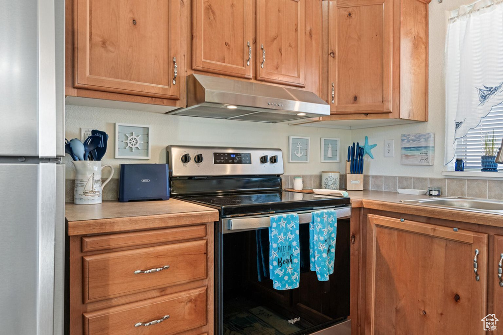 Kitchen with stainless steel appliances, brown cabinets, light countertops, and under cabinet range hood