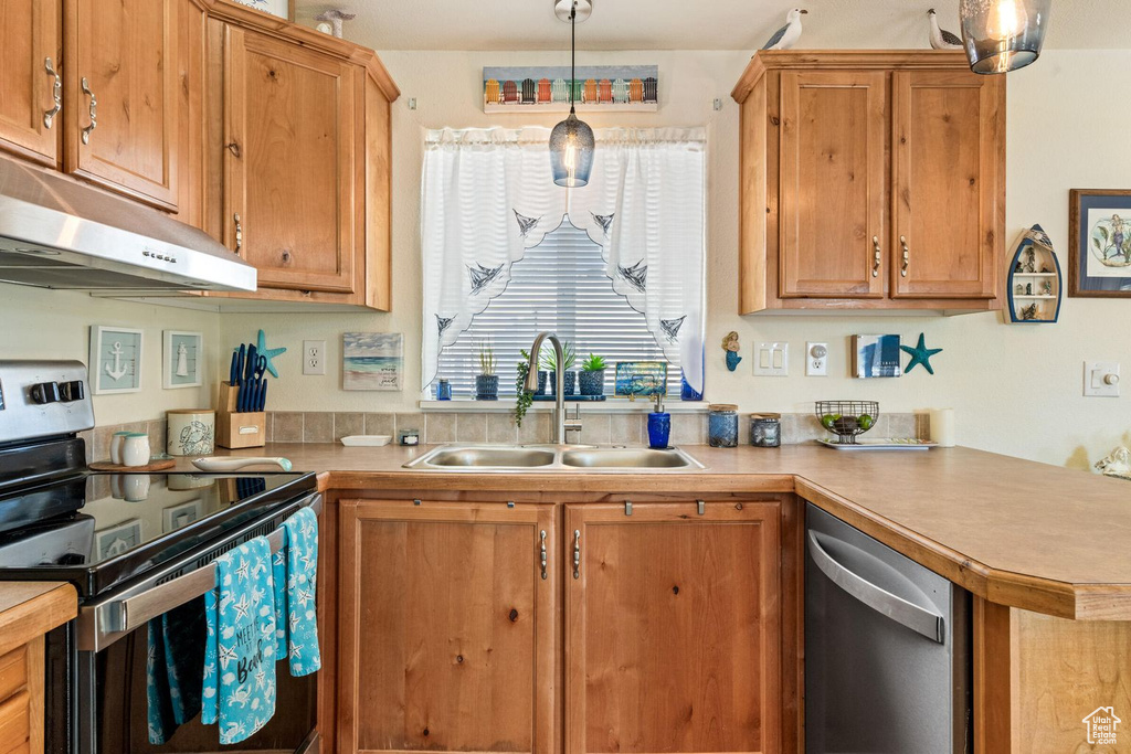 Kitchen featuring decorative light fixtures, light countertops, appliances with stainless steel finishes, a sink, and under cabinet range hood