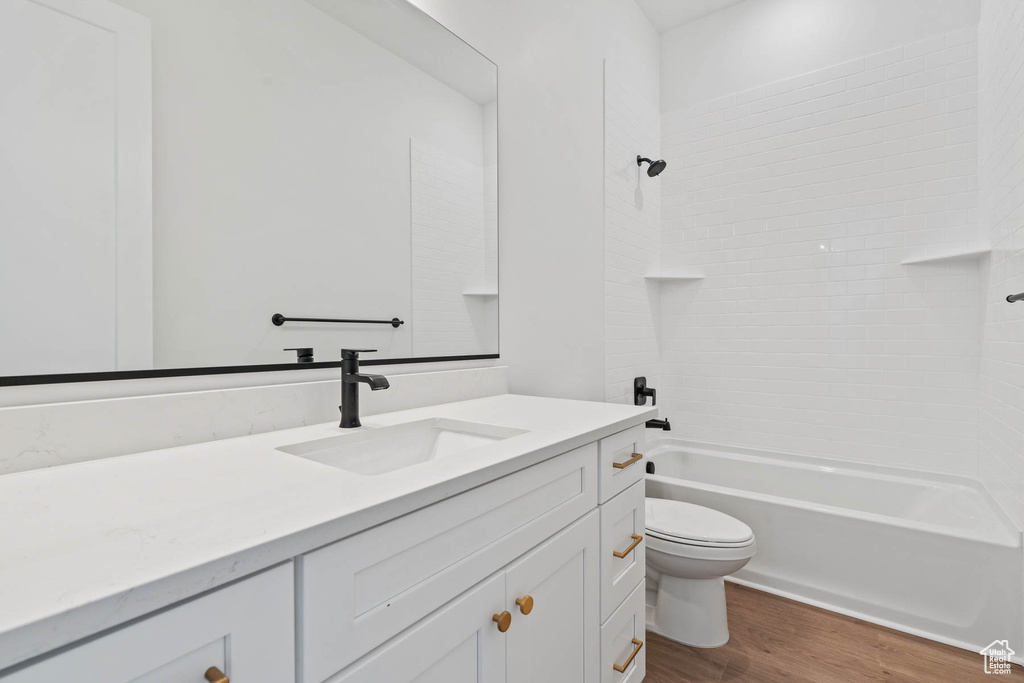 Bathroom with vanity, shower / bath combination, wood finished floors, and toilet