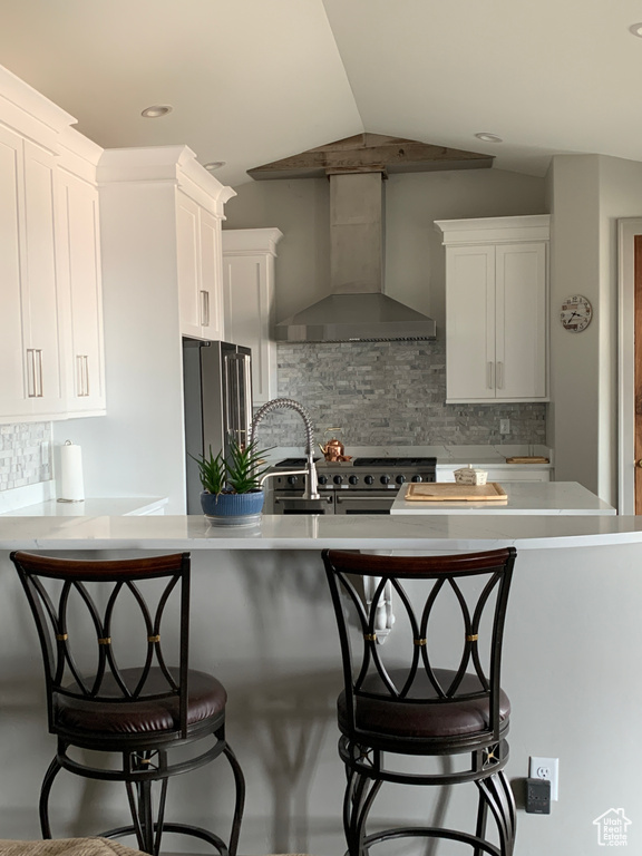 Kitchen with premium appliances, light countertops, white cabinetry, vaulted ceiling, and wall chimney exhaust hood