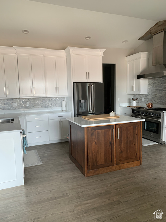 Kitchen with white cabinets, a kitchen island, wood finished floors, stainless steel appliances, and wall chimney range hood