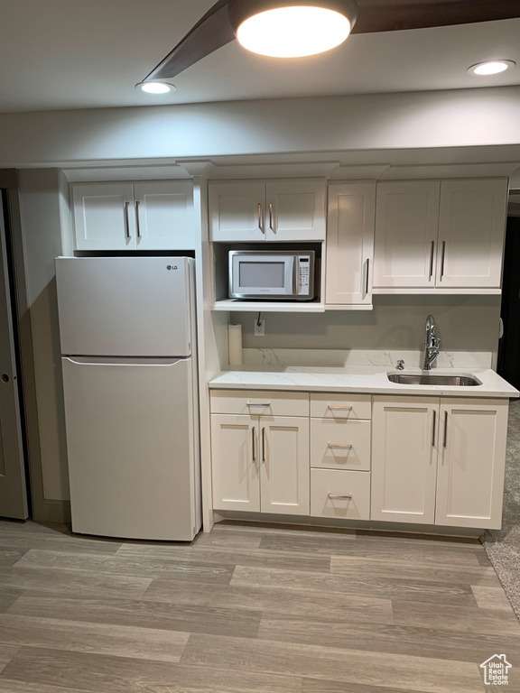 Kitchen featuring light wood finished floors, white appliances, a sink, and recessed lighting