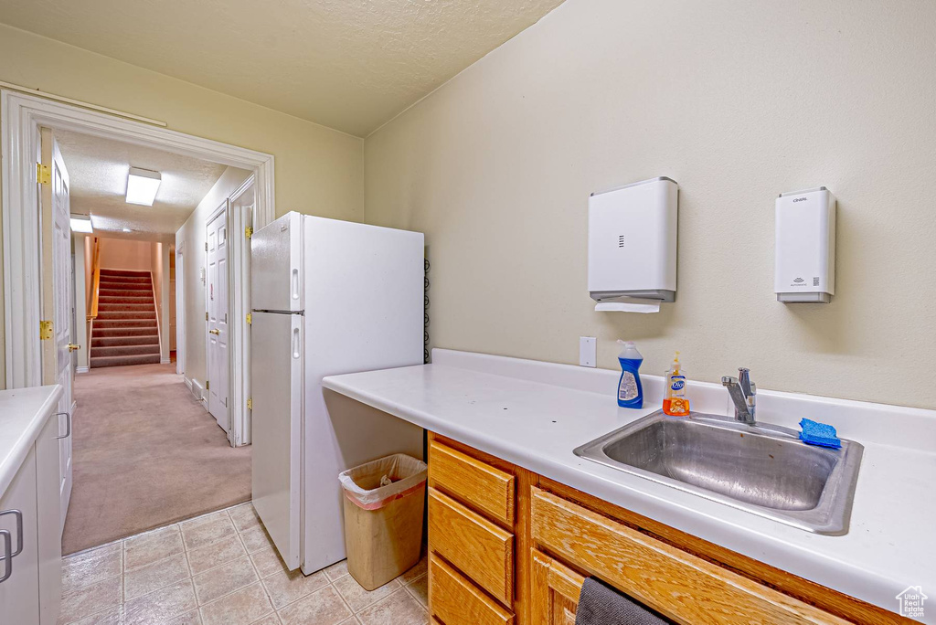 Kitchen with light countertops, brown cabinetry, freestanding refrigerator, a sink, and a textured ceiling