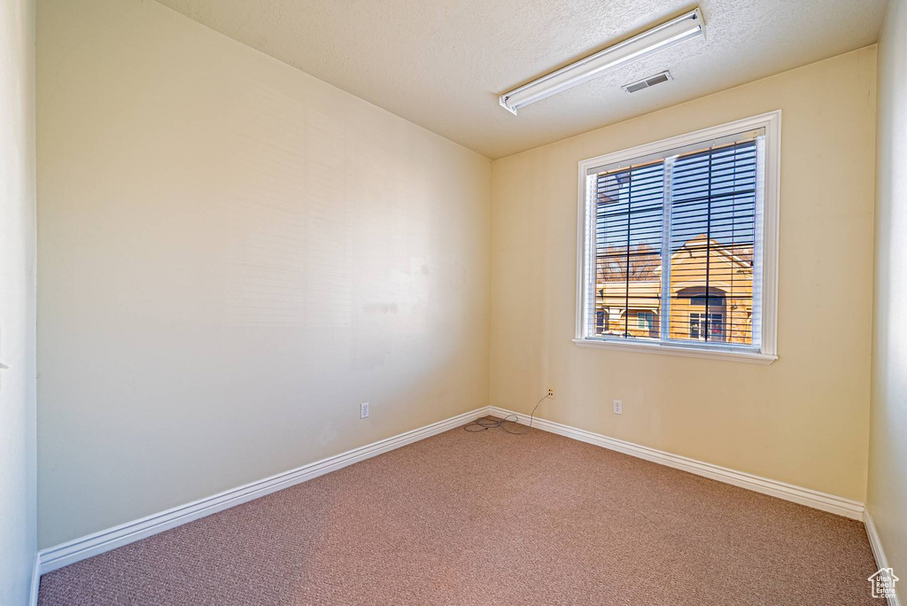 Empty room with carpet, visible vents, a textured ceiling, and baseboards
