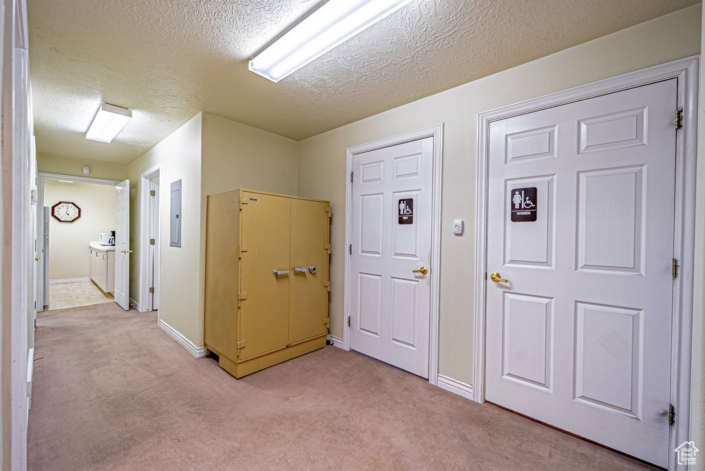 Hallway with a textured ceiling, baseboards, electric panel, and light colored carpet