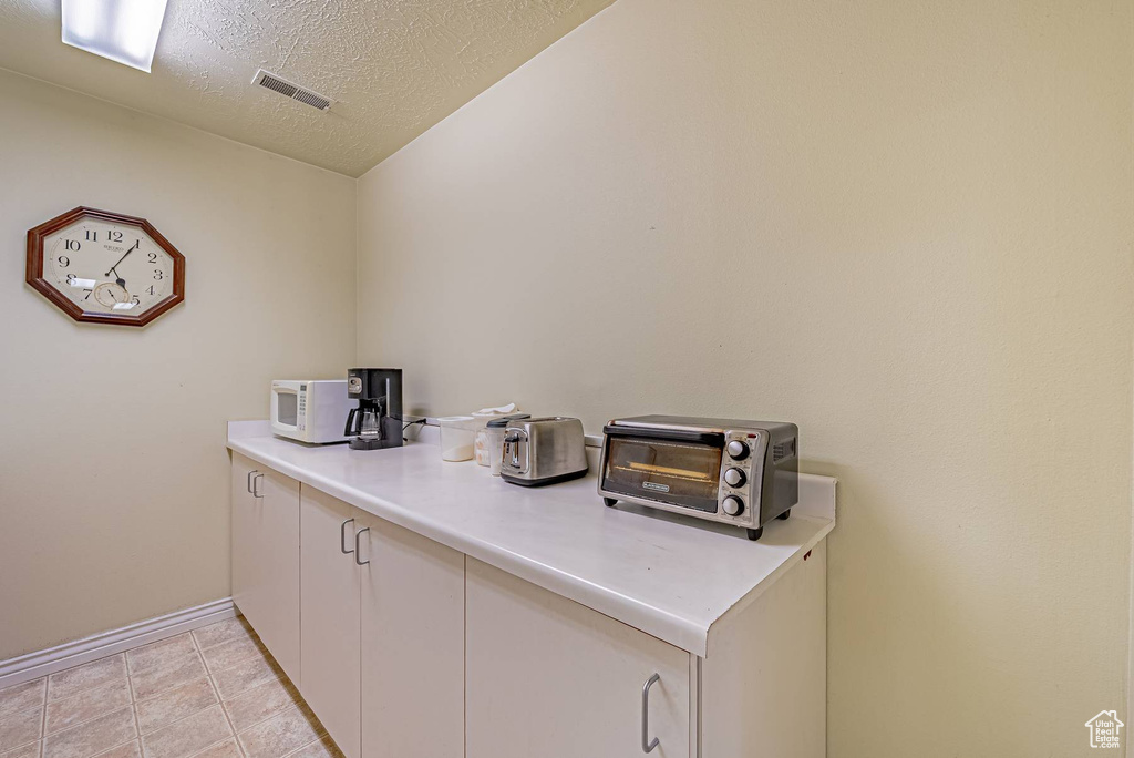 Interior space featuring light tile patterned floors, a toaster, visible vents, baseboards, and a textured ceiling