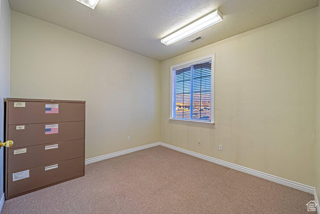Carpeted spare room with visible vents, a textured ceiling, and baseboards