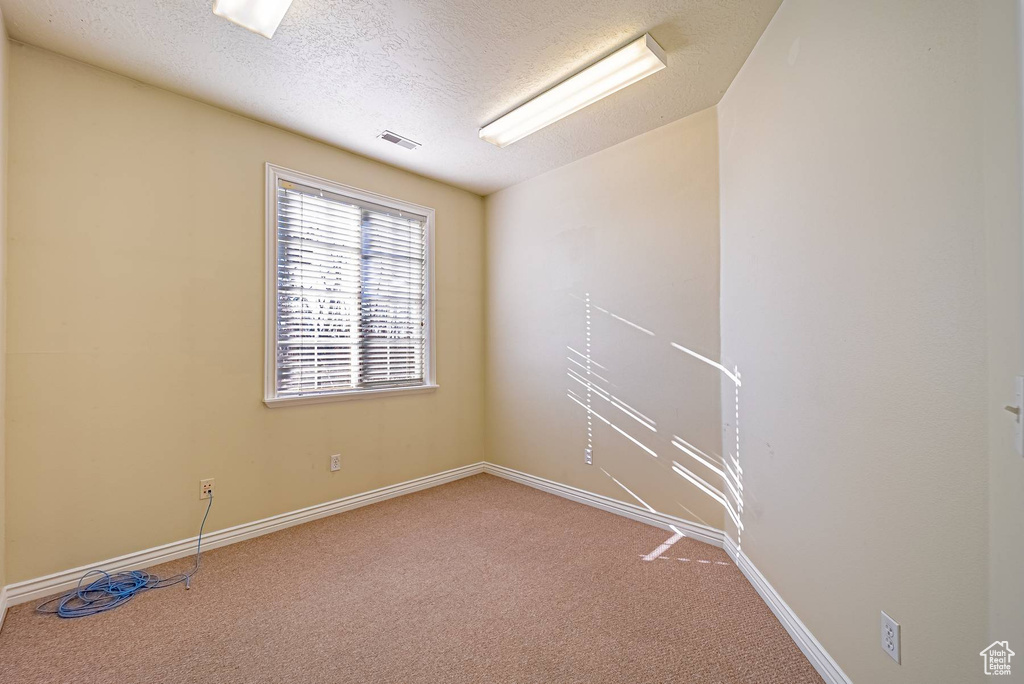 Carpeted empty room featuring visible vents, a textured ceiling, and baseboards