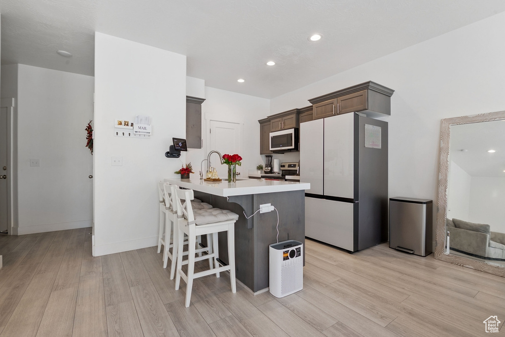 Kitchen featuring a breakfast bar, light countertops, light wood-style floors, freestanding refrigerator, and a peninsula