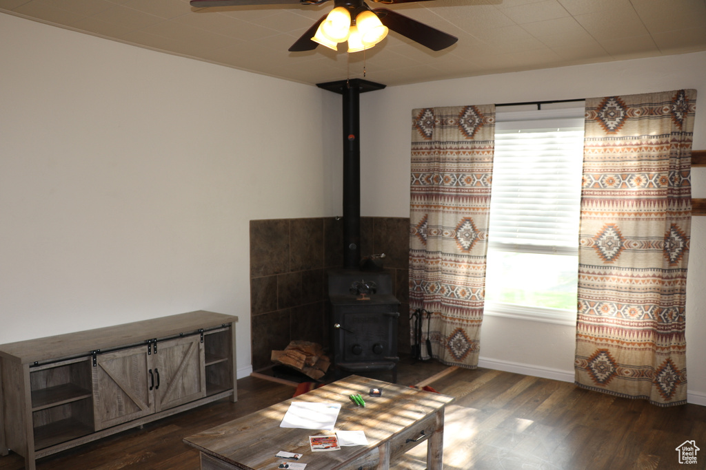 Living room with a wood stove, dark wood-style flooring, ceiling fan, and baseboards