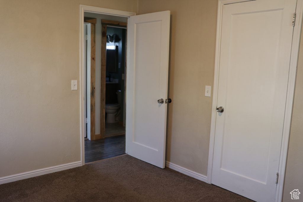 Unfurnished bedroom with dark carpet and baseboards