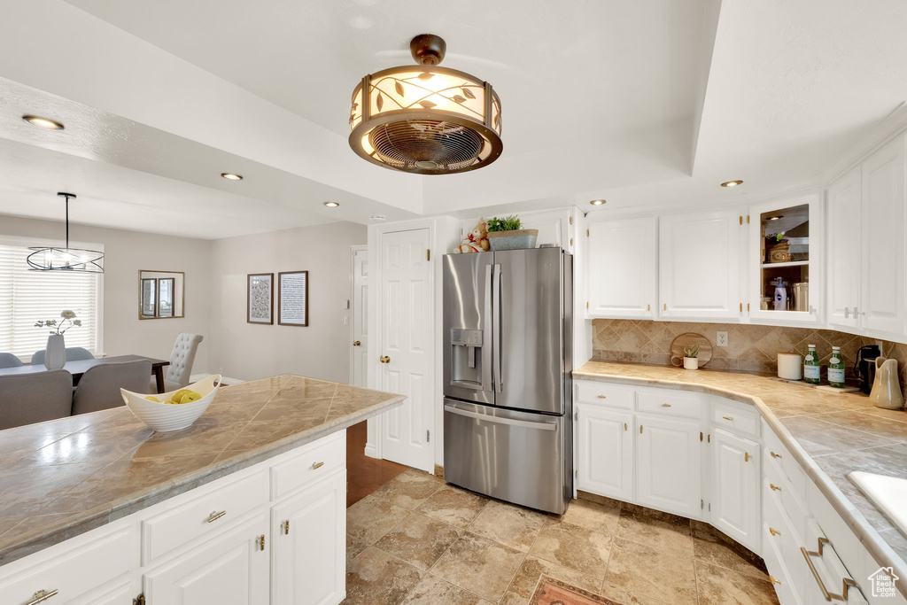 Kitchen with stainless steel refrigerator with ice dispenser, light countertops, white cabinetry, and tasteful backsplash