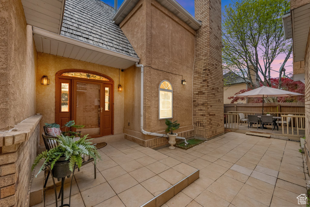 Exterior entry at dusk featuring fence, outdoor dining space, stucco siding, and a chimney
