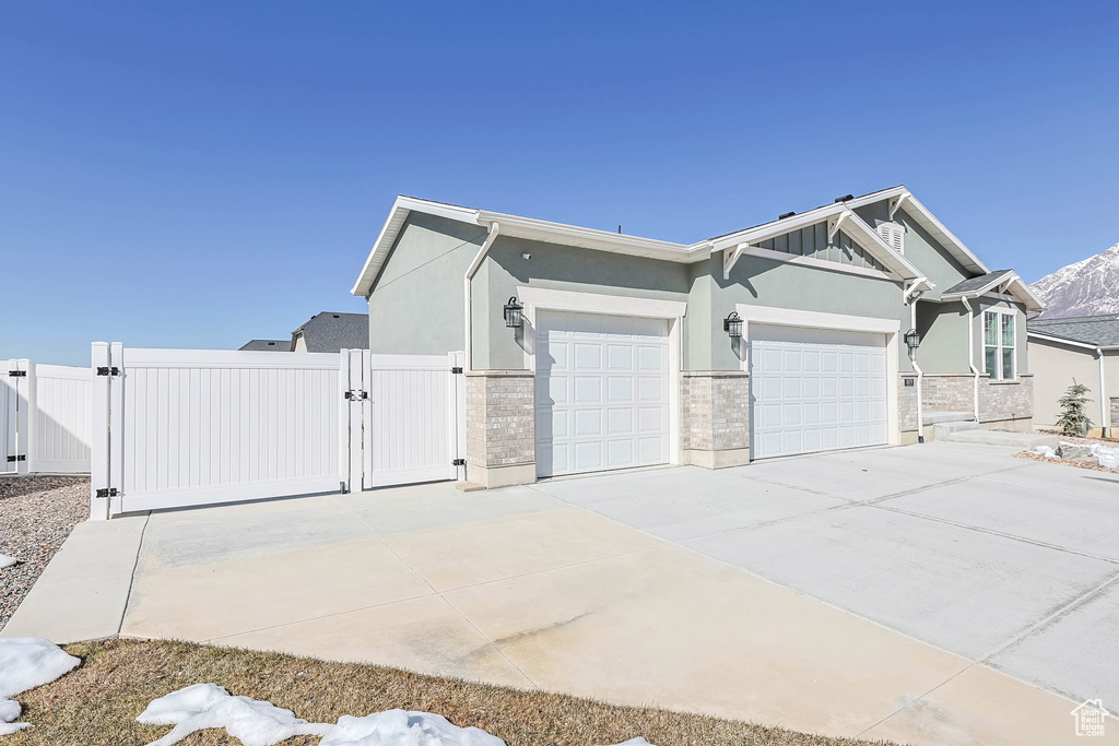 View of side of home featuring stucco siding, a gate, fence, a garage, and driveway