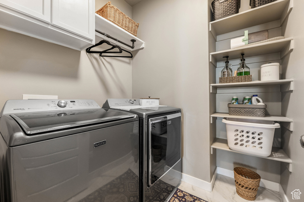 Clothes washing area featuring marble finish floor, washing machine and dryer, cabinet space, and baseboards