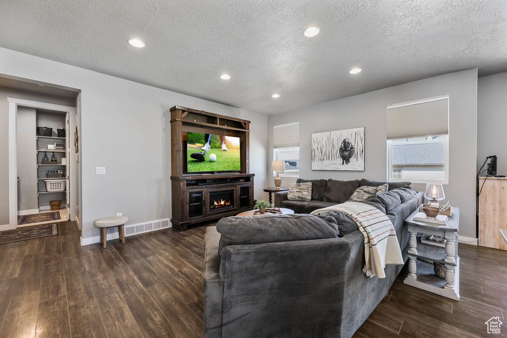 Living room with a warm lit fireplace, recessed lighting, wood finished floors, visible vents, and baseboards