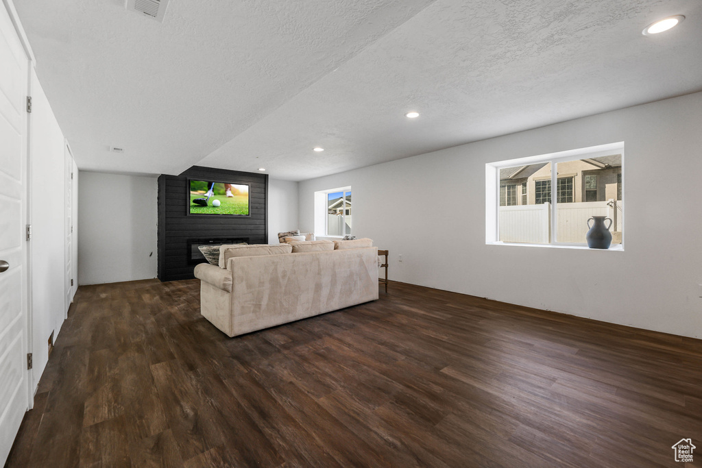 Living room with a textured ceiling, a fireplace, dark wood-type flooring, and recessed lighting