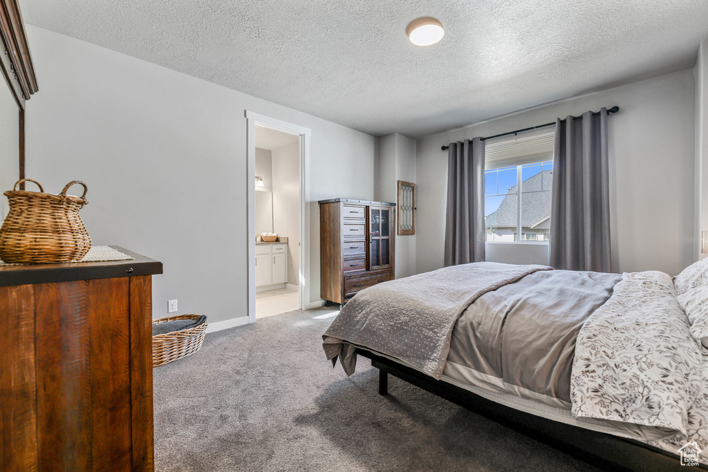 Carpeted bedroom featuring a textured ceiling, baseboards, and ensuite bathroom