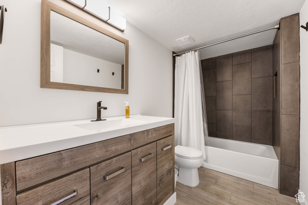 Full bath with shower / bathtub combination with curtain, toilet, a textured ceiling, vanity, and wood finished floors