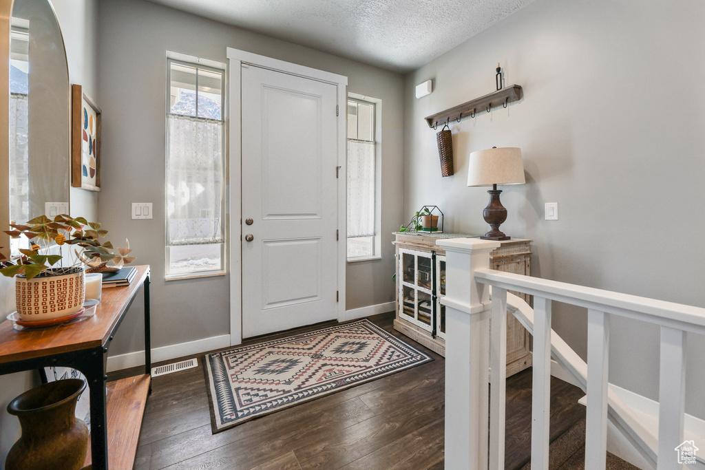 Entryway featuring a textured ceiling, dark wood-type flooring, visible vents, and baseboards