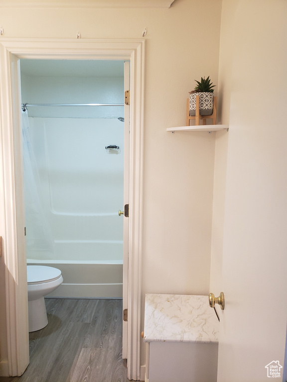 Bathroom featuring shower / washtub combination, wood finished floors, and toilet