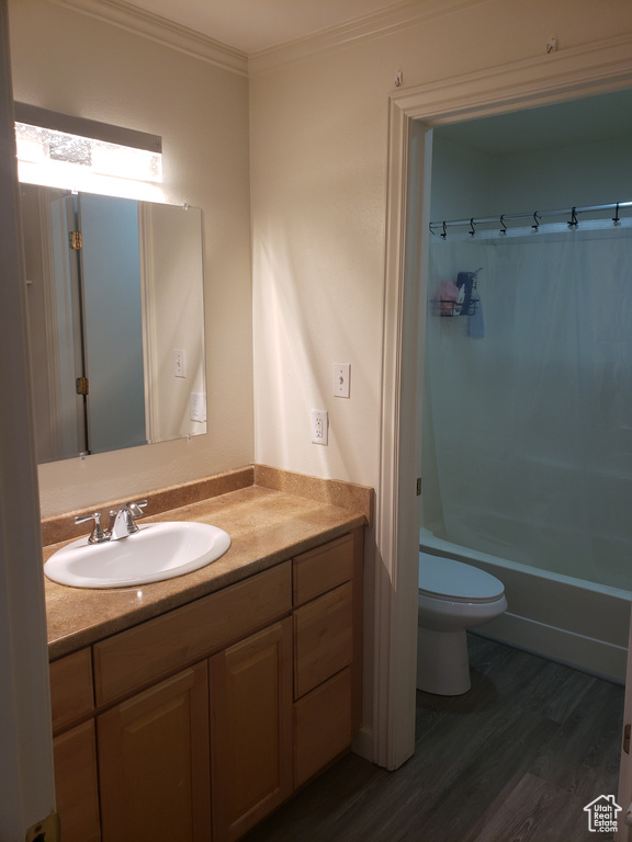 Full bath featuring toilet, ornamental molding, wood finished floors, shower / bath combo with shower curtain, and vanity