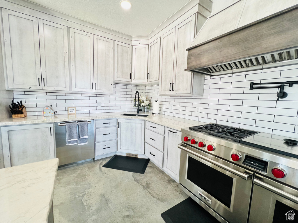 Kitchen featuring a sink, appliances with stainless steel finishes, backsplash, light stone countertops, and wall chimney exhaust hood