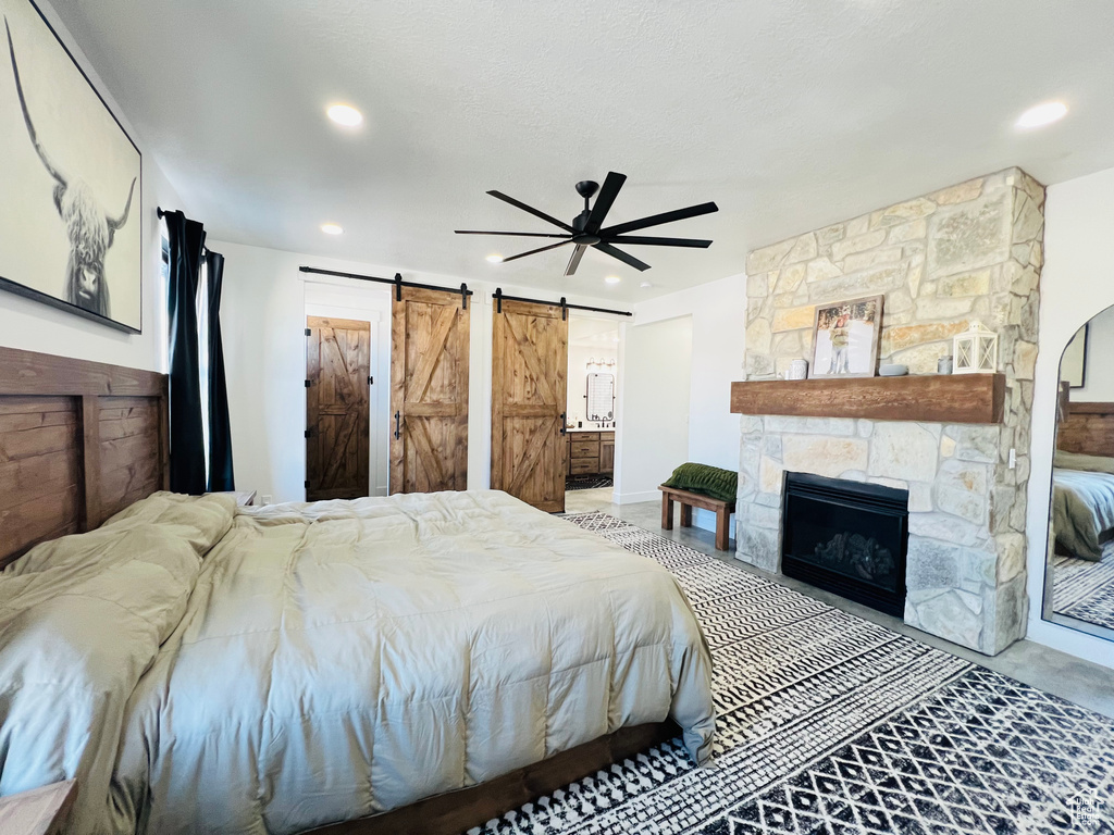 Bedroom with a barn door, a ceiling fan, connected bathroom, a fireplace, and recessed lighting