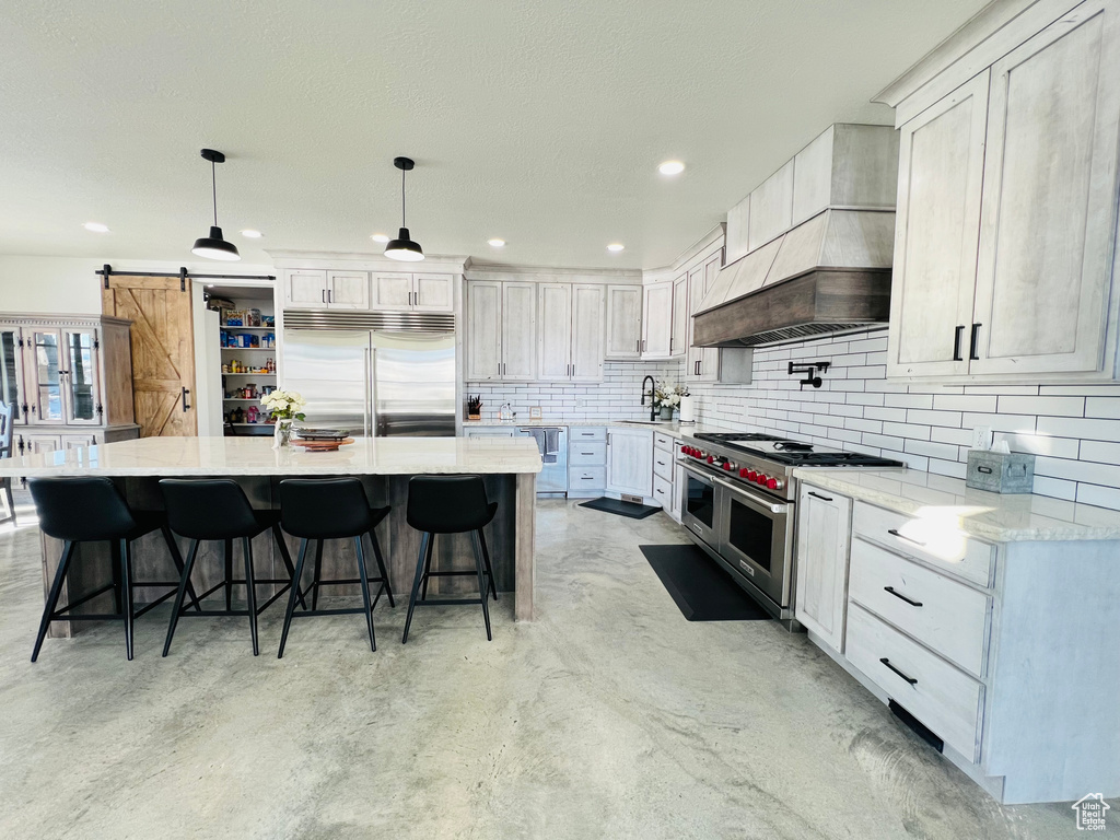 Kitchen with a barn door, high quality appliances, a kitchen breakfast bar, premium range hood, and backsplash