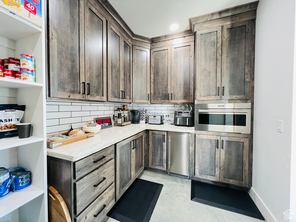 Kitchen featuring oven, dark brown cabinetry, backsplash, and baseboards