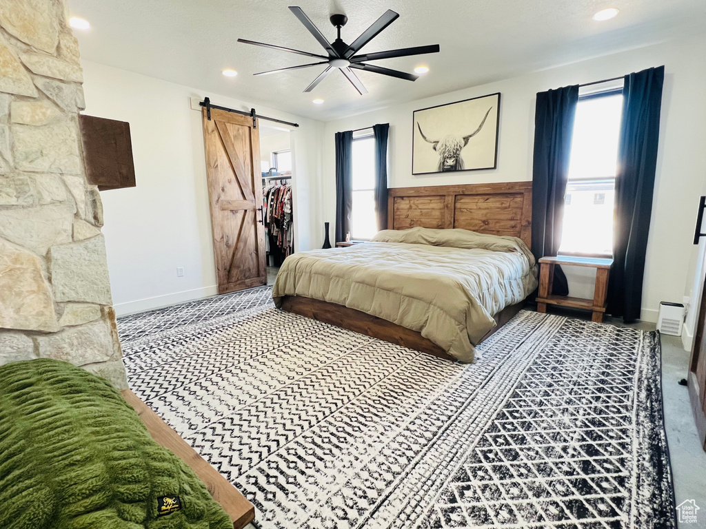 Bedroom with a walk in closet, recessed lighting, a barn door, a ceiling fan, and baseboards