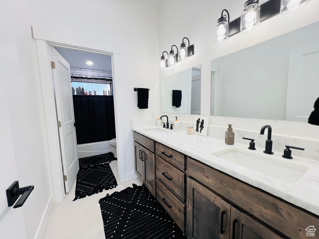 Full bathroom with toilet, double vanity, baseboards, and a sink