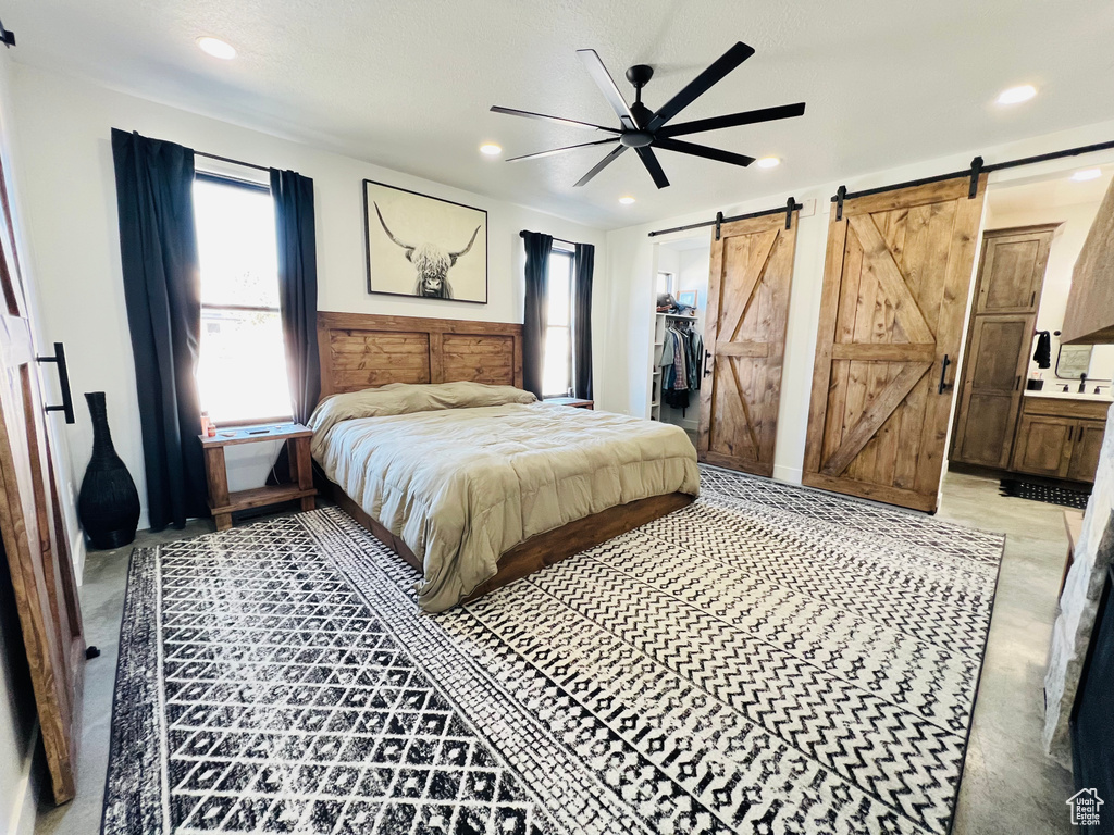 Bedroom with ensuite bath, a barn door, a spacious closet, and recessed lighting