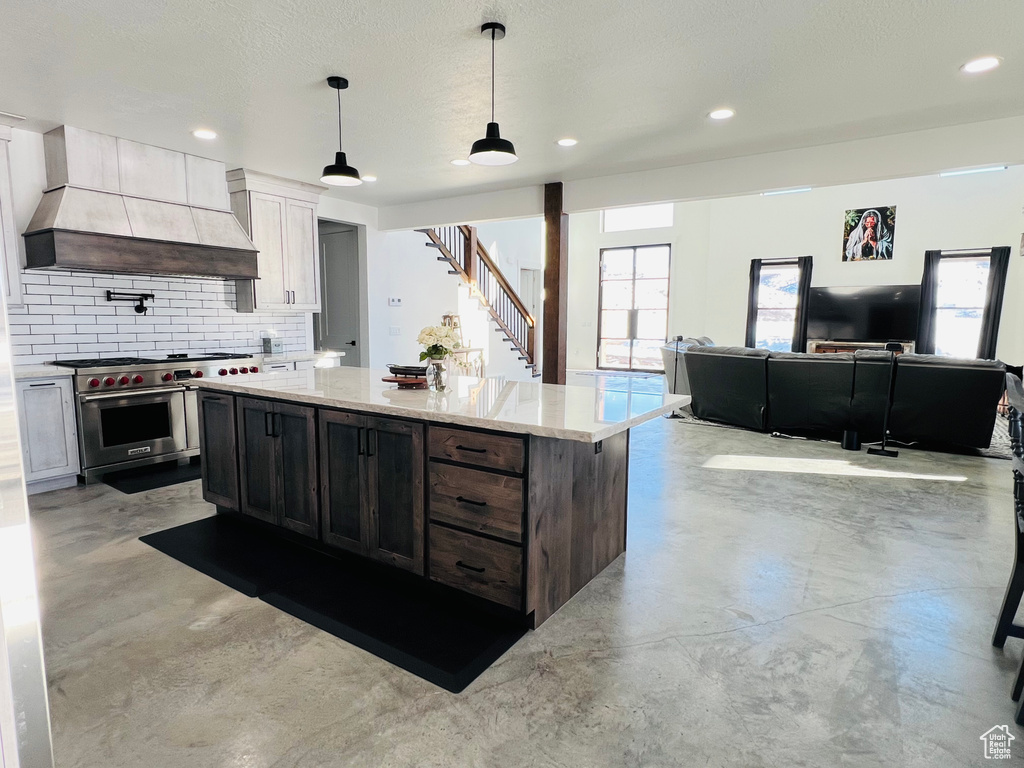 Kitchen featuring light stone counters, tasteful backsplash, premium stove, concrete flooring, and premium range hood