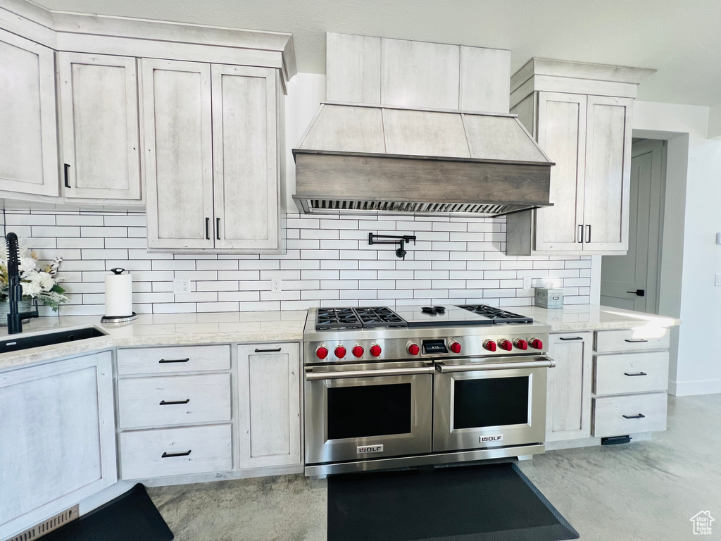 Kitchen featuring a sink, finished concrete floors, custom exhaust hood, double oven range, and backsplash