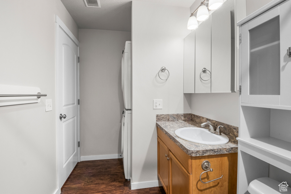 Bathroom with stacked washing machine and dryer, wood finished floors, vanity, baseboards, and toilet