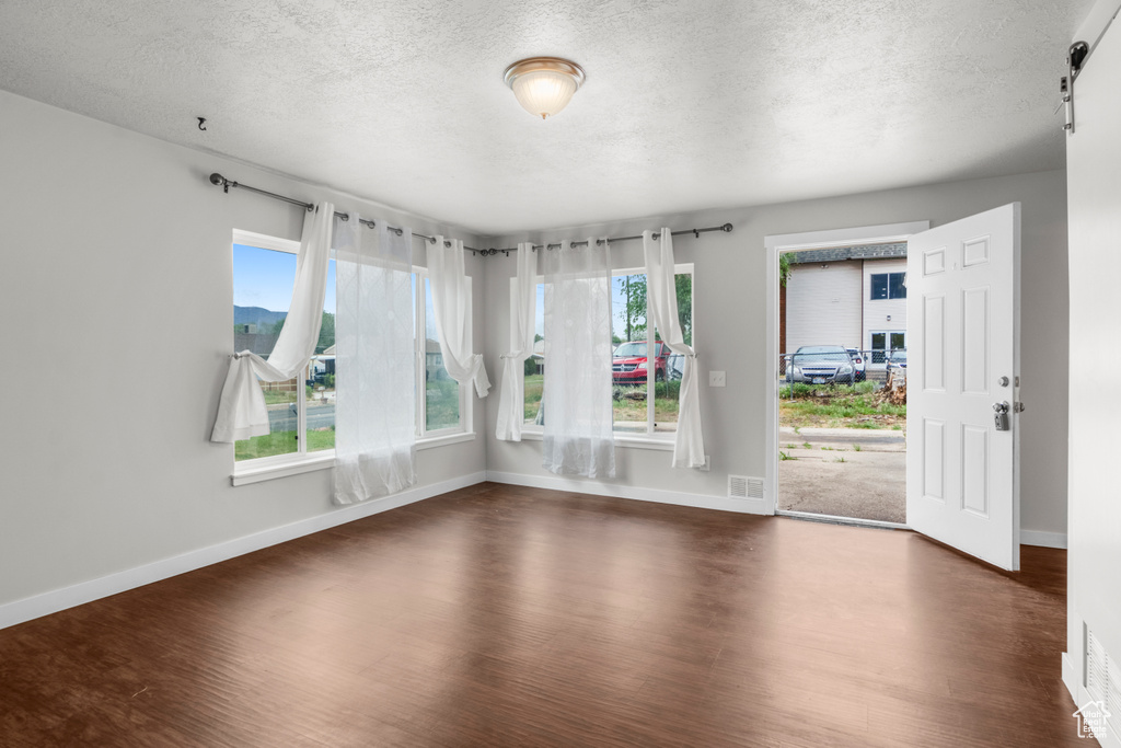 Unfurnished room featuring a textured ceiling, dark wood-type flooring, and baseboards