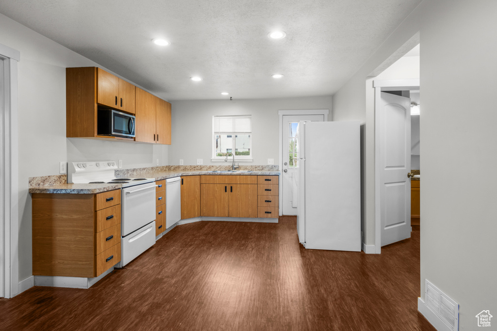 Kitchen with white appliances, a sink, dark wood-style floors, recessed lighting, and light stone countertops
