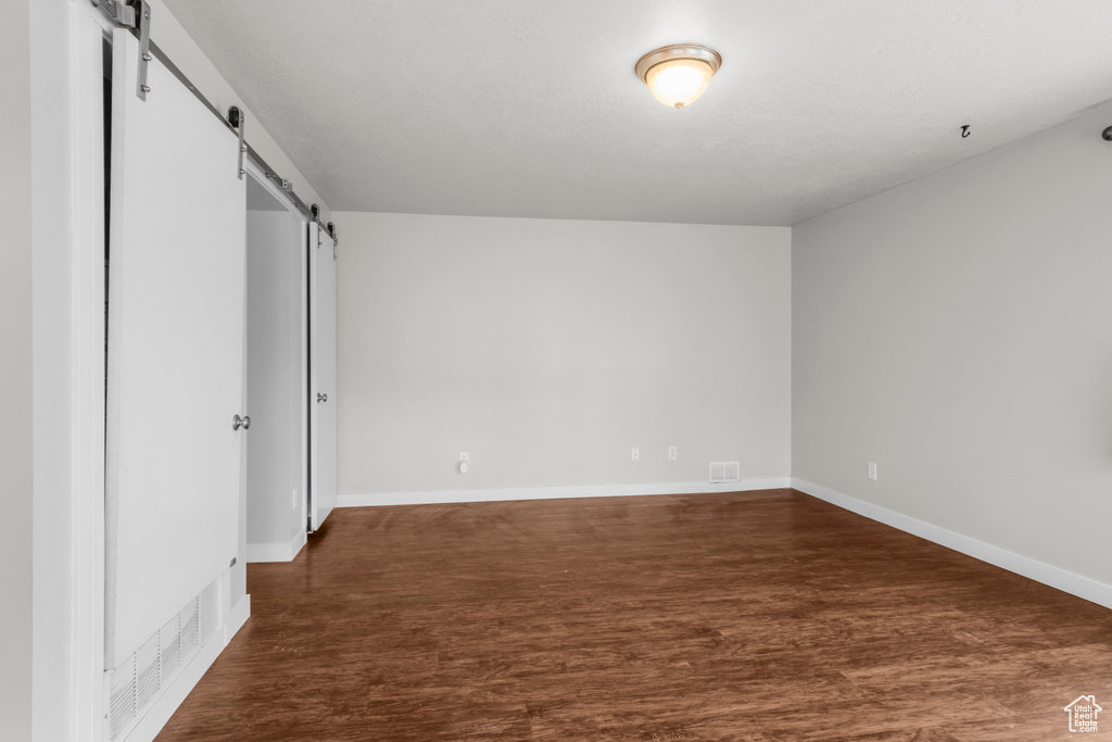 Unfurnished bedroom featuring a barn door, dark wood-style floors, and baseboards