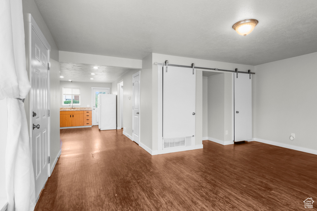 Interior space featuring freestanding refrigerator, a barn door, dark wood-type flooring, and baseboards