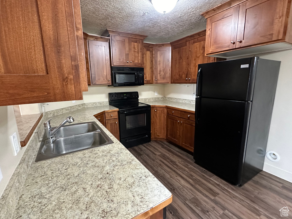 Kitchen with a textured ceiling, dark wood-style flooring, a sink, light countertops, and black appliances
