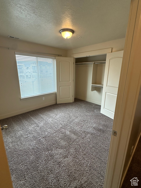 Unfurnished bedroom with a closet, visible vents, carpet flooring, a textured ceiling, and baseboards